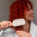 Woman brushing vibrant curly red hair, demonstrating daily care routine for color-treated hair