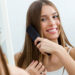 Woman brushing long healthy hair in front of a mirror as part of a premium hair care routine after balayage.