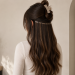 Woman with long dark tape-in hair extensions viewed from the back in a minimalist salon setting, showcasing seamless length, natural volume, and a flawless blend with natural hair.