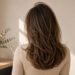 Back view of a woman with fine, layered hair styled for natural volume in a bright, minimalist salon-inspired setting.